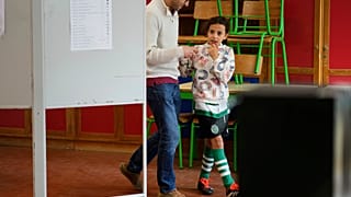 Μια κοπέλα με τη στολή της πρωταθλήτριας Πορτογαλίας Σπόρτινγκ ΚΠ φεύγει από εκλογικό κέντρο μαζί με έναν ψηφοφόρο κατά τη διάρκεια των βουλευτικών εκλογών στην Πορτογαλία