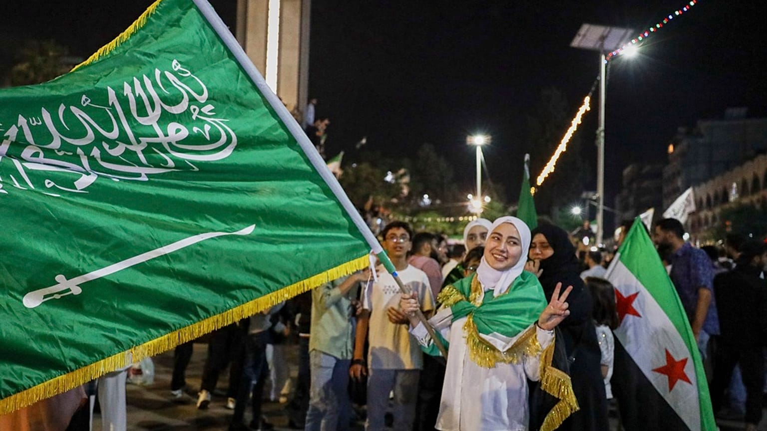 فتاة تحمل العلم السعودي في حمص ، سوريا ، الثلاثاء 13 مايو 2025 ، وهي تحتفل بخطة الرئيس الأمريكي دونالد ترامب لتخفيف العقوبات على سوريا وتطبيع العلاقات مع حكومتها الجديدة.