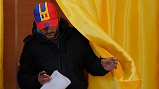 Un uomo esce da una cabina elettorale prima di esprimere il proprio voto al secondo turno delle elezioni presidenziali del Paese a Mogosoaia, 18 maggio 2025.