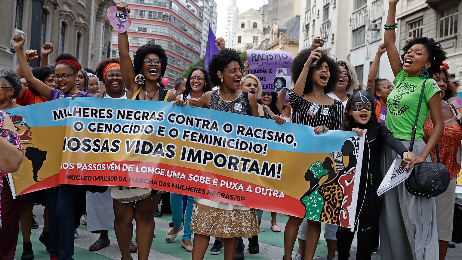 Ativistas marcham com uma faixa onde se lê em português "Mulheres negras contra o racismo, o genocídio e o feminicídio. As nossas vidas importam", durante uma manifestação