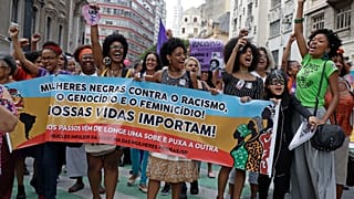 Ativistas marcham com uma faixa onde se lê em português "Mulheres negras contra o racismo, o genocídio e o feminicídio. As nossas vidas importam", durante uma manifestação