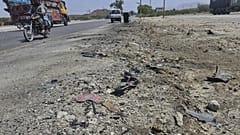 Мотоцикл и другие автомобили проезжают мимо места взрыва, устроенного террористом-смертником на шоссе на окраине города Хуздар на юго-западе Пакистана, 21 мая 2025 года.
