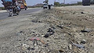Мотоцикл и другие автомобили проезжают мимо места взрыва, устроенного террористом-смертником на шоссе на окраине города Хуздар на юго-западе Пакистана, 21 мая 2025 года.