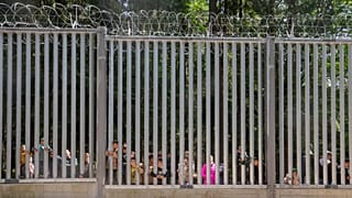 A lengyelországi Bialowiezában 2023. május 28-án, vasárnap egy mintegy 30 fős, menedéket kérő migránscsoport tagjai a Lengyelország által a határon épített fal korlátján keresztül néznek át.
