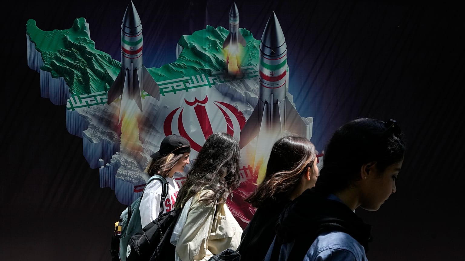 Iranische Frauen gehen an einem Transparent vorbei, das den Abschuss von Raketen von einer iranischen Landkarte in Teheran zeigt, 19. April 2024