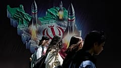 Des femmes iraniennes passent devant une banderole montrant des missiles lancés depuis une carte iranienne à Téhéran, le 19 avril 2024.
