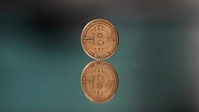 Uma ficha de uma bitcoin reflecte-se quando é colocada num espelho em Praga, República Checa, domingo, 11 de maio de 2025.