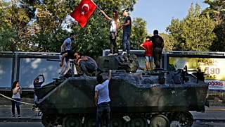 Vatandaşlar, Ankara'daki askeri karargaha yakın bir sokakta protestocular tarafından saldırıya uğrayan hasarlı bir tankın üstünde