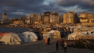 نازحون فلسطينيون يمشون في مخيم مؤقت في ميناء مدينة غزة يوم الخميس 22 أيار / مايو 2025.