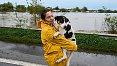 Eine Frau trägt einen Hund entlang einer überfluteten Autobahn nach starken Regenfällen in Campana, Argentinien, am Samstag, den siebzehnten Mai zweitausendfünfundzwanzig.