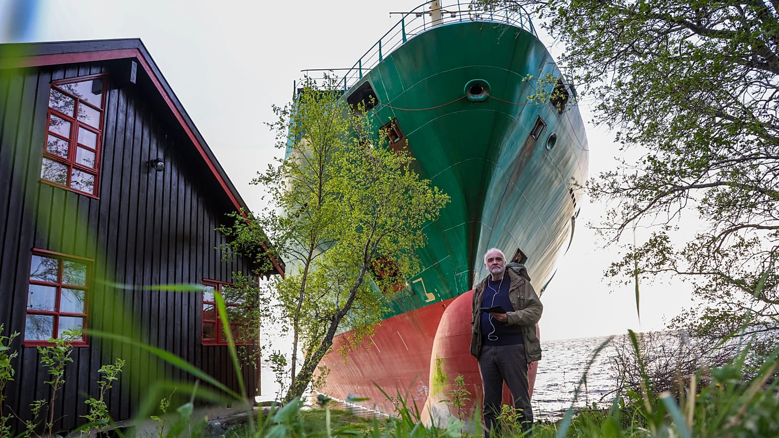 Johan Helberg ao lado da sua casa com o navio porta-contentores NCL Salten ao fundo no Trondheimsfjord, 22 de maio de 2025 