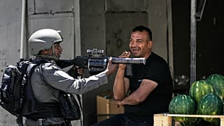عنصر من شرطة حرس الحدود الإسرائيلية يتمركز بجوار بائع بطيخ خلال مداهمة عسكرية في مخيم عسكر قرب مدينة نابلس – الثلاثاء 20 أيار/مايو 2025. 