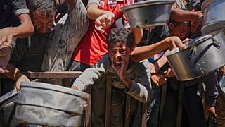 فلسطينيون يحاولون الحصول على وجبات من مطبخ مجتمعي في منطقة المواصي بخان يونس، غزة – الجمعة 23 أيار/مايو 2025.