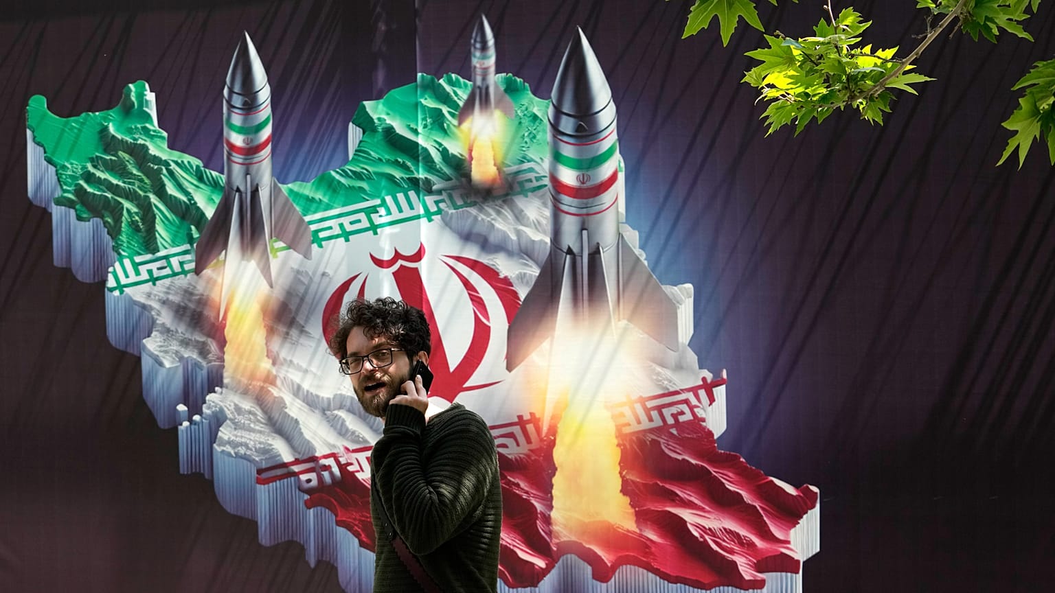 Um transeunte passa por um cartaz que mostra mísseis a serem lançados do mapa iraniano no norte de Teerão, 19 de abril de 2024