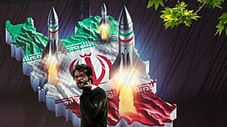 Um transeunte passa por um cartaz que mostra mísseis a serem lançados do mapa iraniano no norte de Teerão, 19 de abril de 2024
