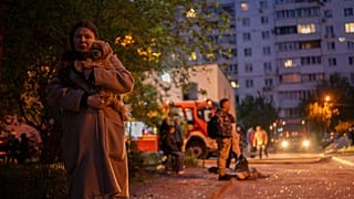 امرأة تحمل كلبها وهي تمشي في شارع مع قطع من الزجاج المكسور في موقع مبنى سكني تضرر بعد هجوم روسي في كييف ، أوكرانيا ، السبت 24 مايو 2025.
