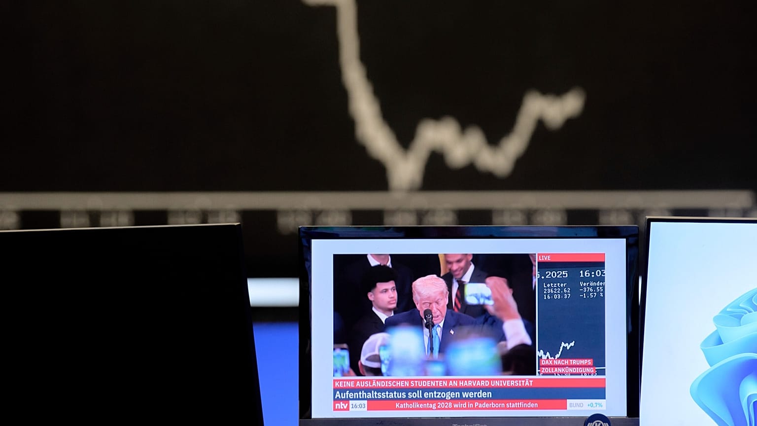 The curve of the German stock index DAX is seen in the background as US President Donald Trump is shown on a TV screen at the stock market in Frankfurt, 23 May 2025