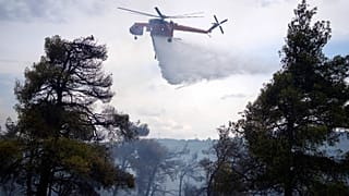 A helicopter drops water over a woodland during a wildfire in the suburb of Stamata, in northern Athens, Greece, Sept. 4, 2023.