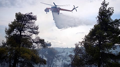 A helicopter drops water over a woodland during a wildfire in the suburb of Stamata, in northern Athens, Greece, Sept. 4, 2023. 