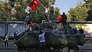 Vatandaşlar, Ankara'daki askeri karargaha yakın bir sokakta protestocular tarafından saldırıya uğrayan hasarlı bir tankın üstünde