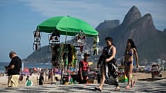 Sahile gidenler Rio de Janeiro'daki Ipanema Plajı'nda plaj kıyafetleri satan bir satıcının standının önünden geçiyor.