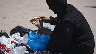 إسلام أبو طعيمة، أم لخمسة أطفال تبلغ من العمر 40 عامًا، بالتقاط قطعة خبز من كومة قمامة في مدينة غزة، يوم الأحد 25 مايو 2025