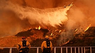 Os bombeiros observam um helicóptero a lançar água sobre o incêndio de Palisades em Mandeville Canyon, em Los Angeles.