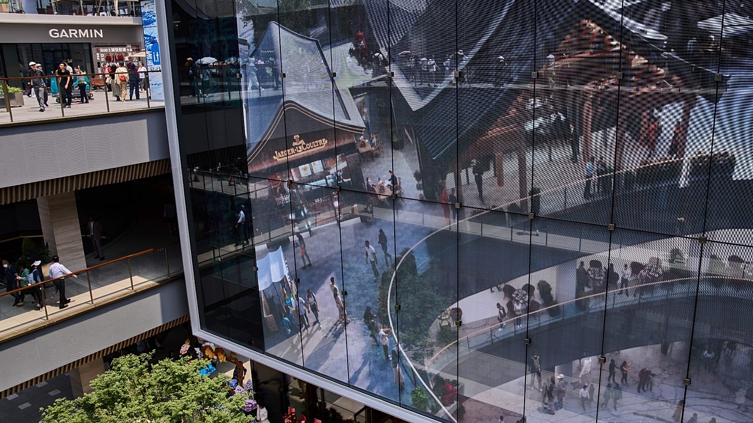 İnsanlar 26 Mayıs 2025, Pazartesi günü Pekin'de yeni açılan Hutong tarzı açık hava alışveriş merkezini tanıtan bir projektör ekranının önünde tur atıyor.