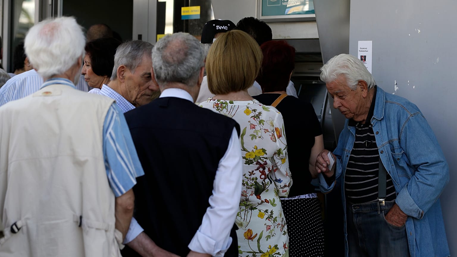 Συνταξιούχος περιμένει να μπει σε τράπεζα, ενώ άλλοι στέκονται στην ουρά για να χρησιμοποιήσουν το ΑΤΜ του υποκαταστήματος στην Αθήνα
