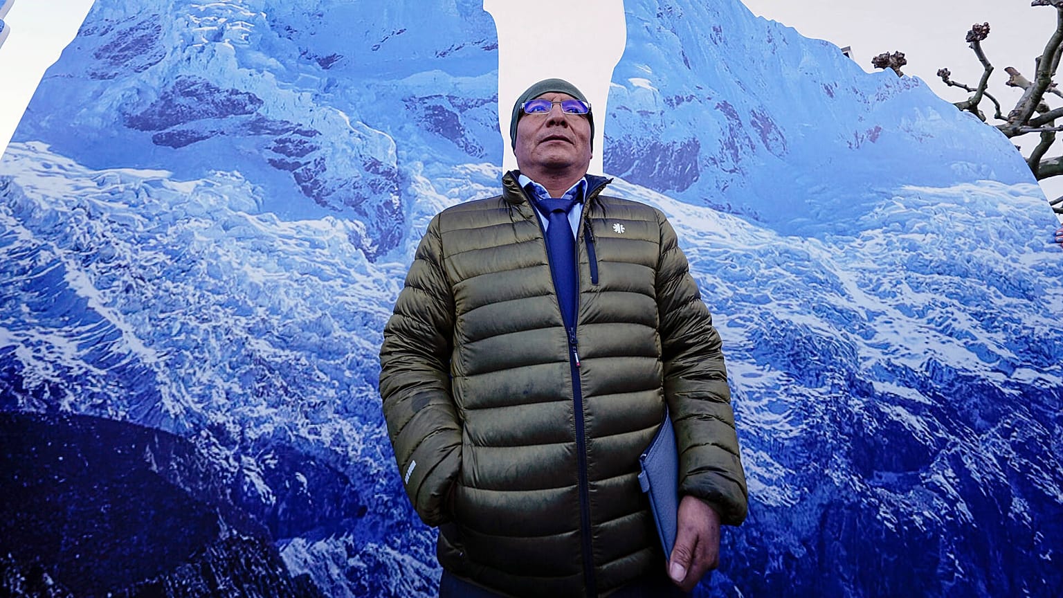 The plaintiff Peruvian farmer Luciano Lliuya stands in front of glacier pictures held by activists at the Higher Regional Court in Hamm, Germany. 