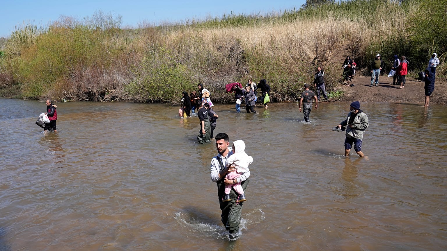 Famílias sírias alauítas atravessam um rio que marca a fronteira entre a Síria e o Líbano na província de Akkar, 11 de março de 2025