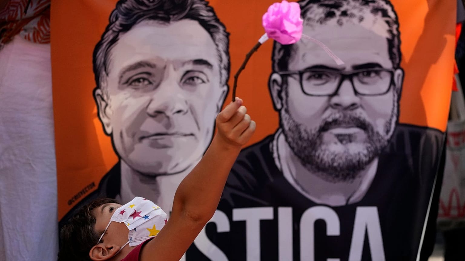 Um rapaz brinca com uma flor em frente a uma faixa com imagens do jornalista britânico Dom Phillips, à esquerda, e do especialista em questões indígenas Bruno Pereira, em junho de 2022.