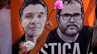 Um rapaz brinca com uma flor em frente a uma faixa com imagens do jornalista britânico Dom Phillips, à esquerda, e do especialista em questões indígenas Bruno Pereira, em junho de 2022.