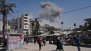 O fumo eleva-se no céu após um ataque aéreo israelita, enquanto os palestinianos caminham na cidade de Gaza, 30 de maio de 2025