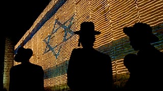 رجال يهود أرثوذكس متطرفون يمشون أمام علم كبير مصنوع من الأضواء على جدار البلدة القديمة في القدس 