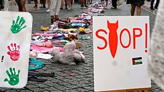 Pessoas passam por uma instalação de roupas e brinquedos de criança espalhados pela baixa de Lisboa, para chamar a atenção para a situação das crianças em Gaza