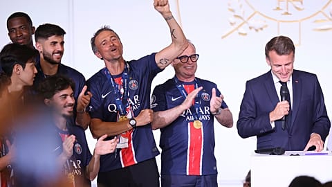 French President Emmanuel Macron, right, speaks while PSG's head coach Luis Enrique clinches his fist during a ceremony at the Elysee. Palace after the team won the Champions 
