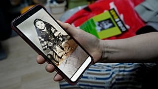 ARCHIVO - Una mujer sostiene un teléfono que muestra una foto de su hijo, desaparecido en 1975, mientras está sentada en su habitación de motel en Seúl, 5 de marzo de 2024.