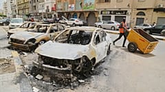 Ağır silahlı milisler arasında çıkan çatışmaların ardından yanmış arabaların yanından geçen bir adam, Trablus, 15 Mayıs 2025.