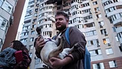 Ein Mann trägt seinen Hund vor einem Wohnhochhaus, das nach einem russischen Drohnenangriff auf Kyjiw, Ukraine, am Freitag, den 6. Juni 2025, beschädigt wurde.