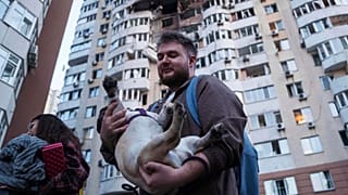 A man carries his dog in front of a residential multi-storey building damaged after a Russian drone strike on Kyiv, Ukraine, on Friday, June 6, 2025. 