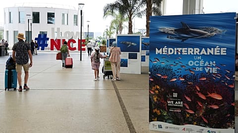 Des personnes quittent l'aéroport à proximité de panneaux annonçant la prochaine conférence des Nations unies sur les océans, qui se tiendra à Nice.
