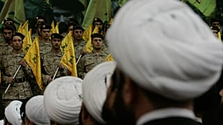 رجال دين شيعة لبنانيون يجلسون أمام مقاتلي حزب الله أثناء مشاركتهم في تجمع إحياءً لذكرى القائد العسكري البارز في حزب الله عماد مغنية، يوم الجمعة 22 فبراير/شباط 2008. 