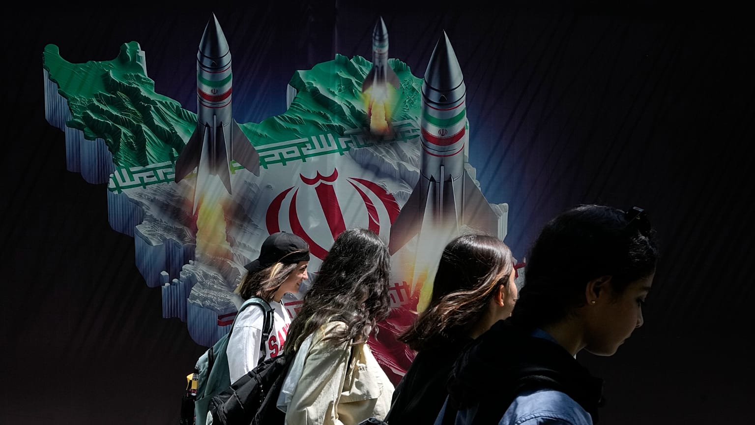 Iranische Frauen gehen an einem Transparent vorbei, das den Abschuss von Raketen von der iranischen Landkarte im Norden Teherans zeigt, 19. April 2024
