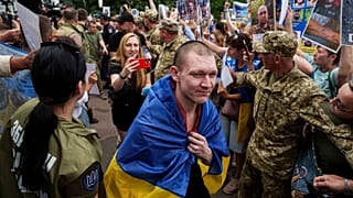 Um soldado ucraniano caminha por um corredor humano com pessoas segurando fotos dos seus familiares desaparecidos, na região de Chernyhiv, Ucrânia, 9 de junho de 2025
