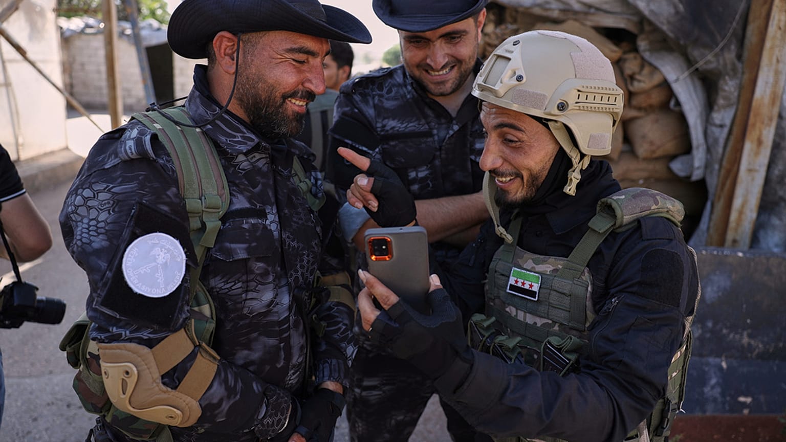 أحد أفراد قوات الأمن الحكومية، على اليمين، يضحك مع مقاتلين من قوات سوريا الديمقراطية التي يقودها الأكراد خلال تبادل للأسرى في حي الشيخ مقصود