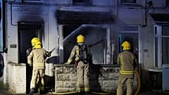 Einsatzkräfte arbeiten vor einem Haus in Ballymena, Nordirland, während Menschen am Dienstag, den zehnten Juni zweitausendfünfundzwanzig, gegen einen mutmaßlichen sexuellen Übergriff in der Stadt Co Antrim protestieren.