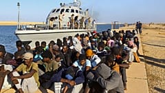  صورة لمهاجرين تم إنقاذهم بجوار قارب لخفر السواحل في مدينة الخمس الليبية، على بُعد حوالي 120 كيلومترًا (75 ميلًا) شرق طرابلس. 
