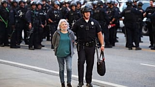 Un agente de la ley escolta a una mujer fuera de una protesta después de ser detenida el miércoles 11 de junio de 2025, en Los Ángeles