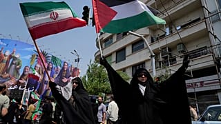 Manifestantes iranianos seguram bandeiras iranianas e palestinianas numa manifestação anti-Israel em Teerão, Irão, sexta-feira, 13 de junho de 2025.